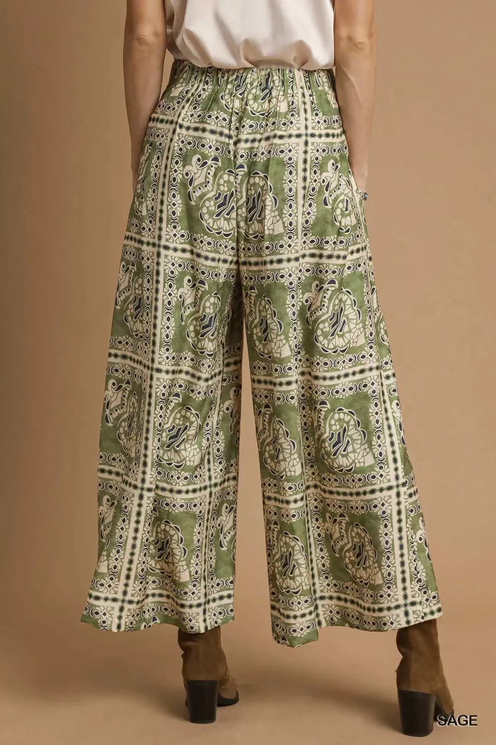 Model wearing Sage Mosaic Boho Pants with sage-toned bohemian print, wide-leg silhouette, and functional side pockets styled with boots.