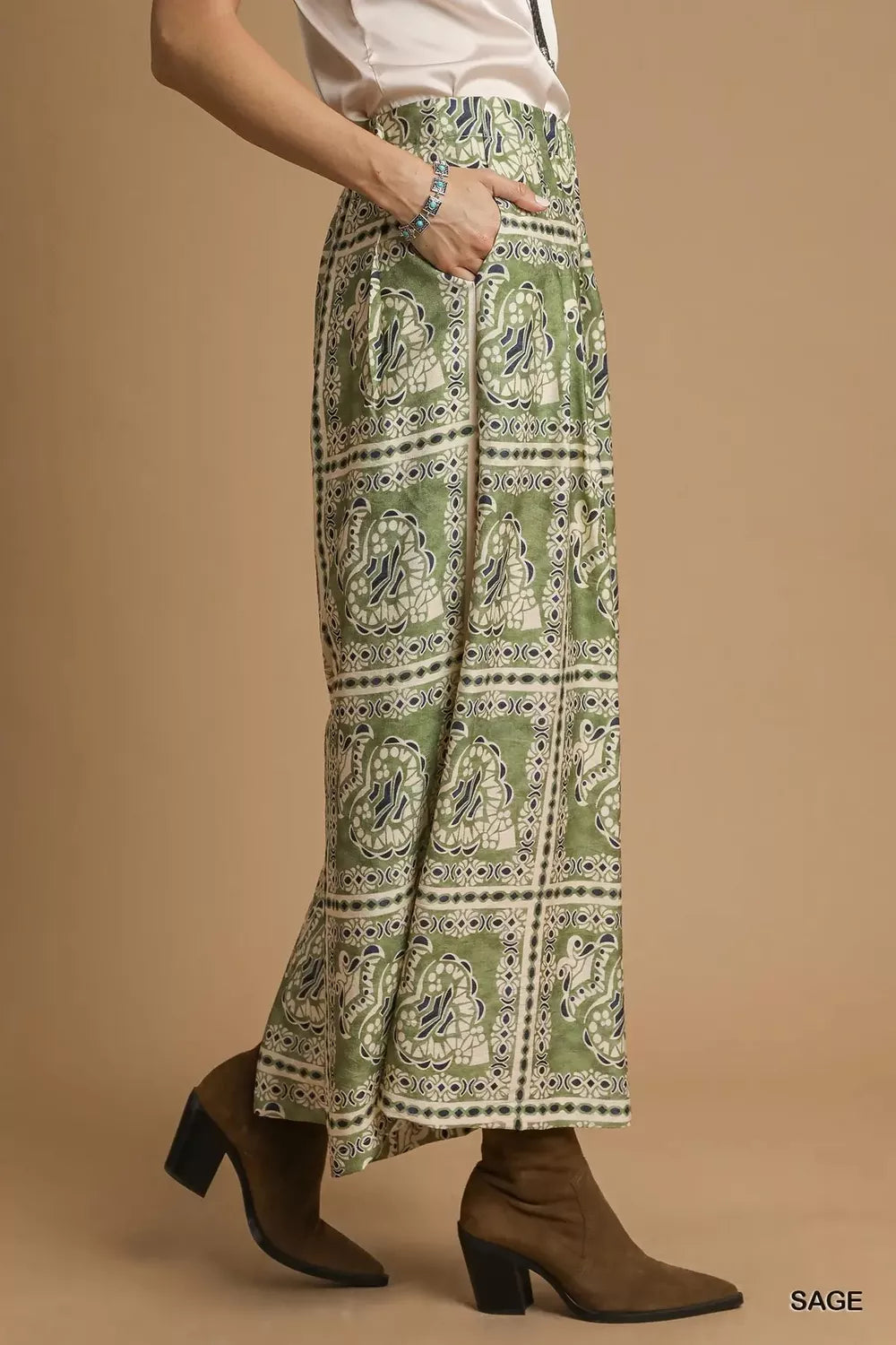 Model wearing Sage Mosaic Boho Pants with sage-toned bohemian print, wide-leg silhouette, and functional side pockets styled with boots.