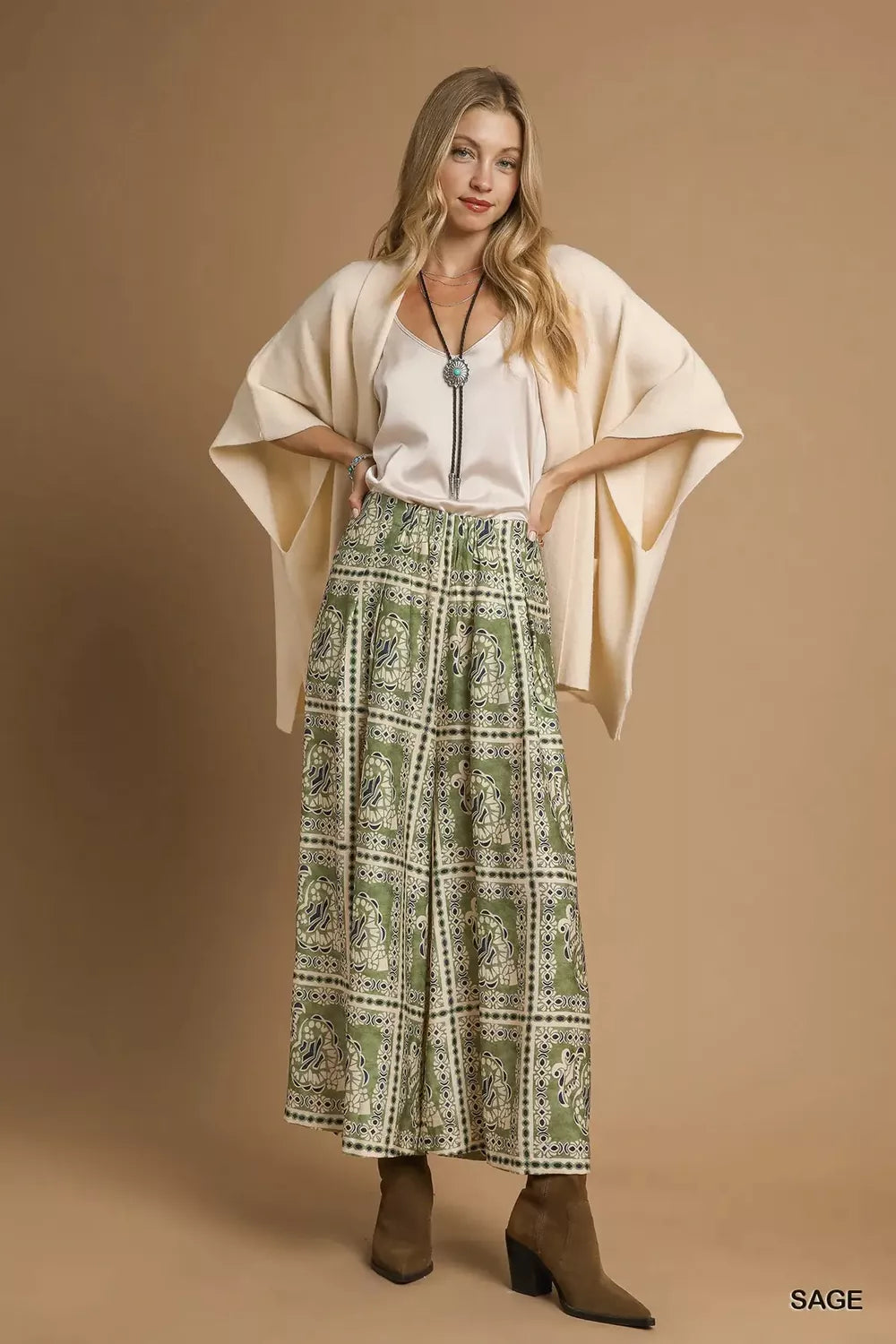 Model wearing Sage Mosaic Boho Pants with sage-toned bohemian print, wide-leg silhouette, and functional side pockets styled with boots.