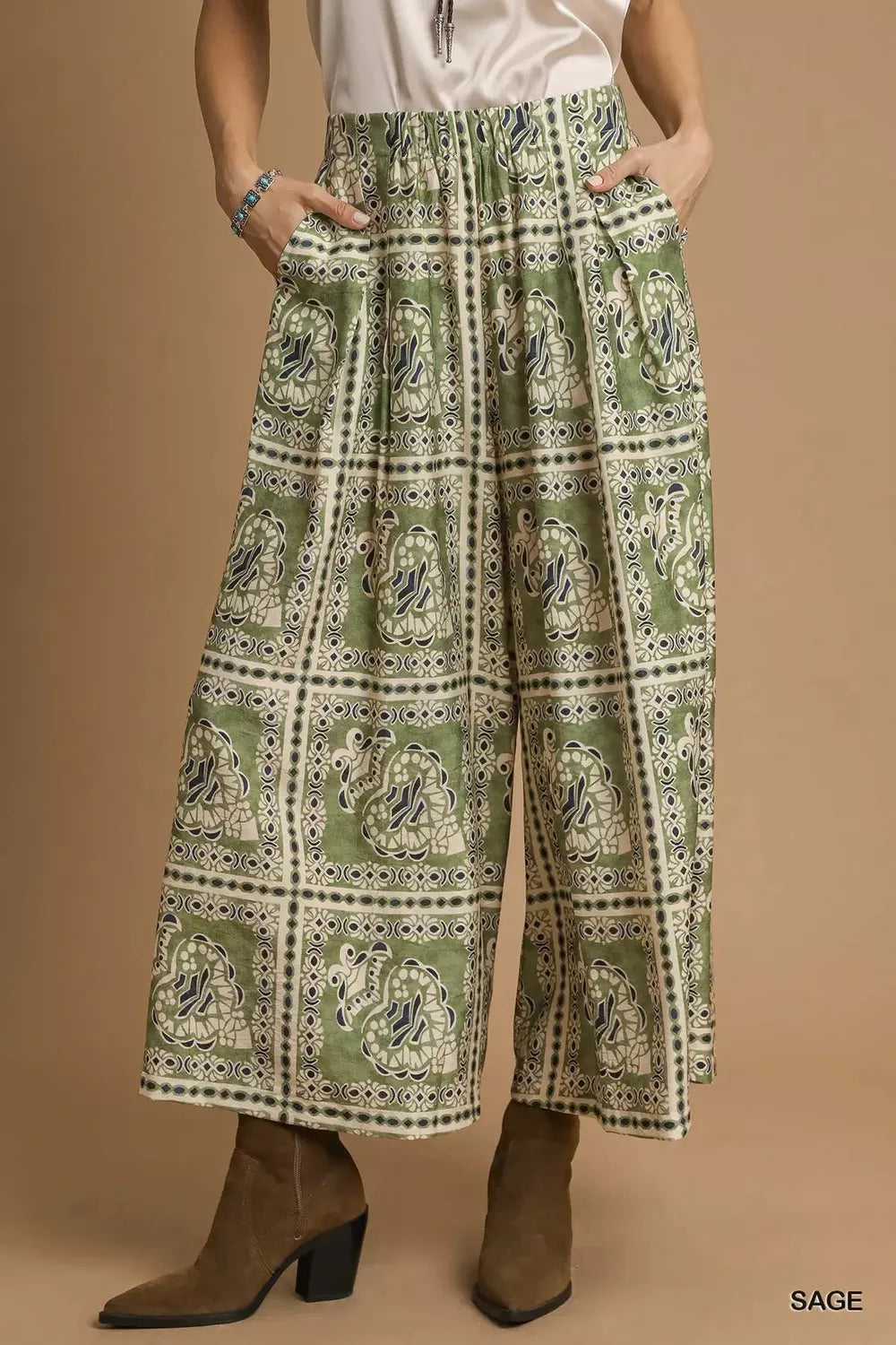 Model wearing Sage Mosaic Boho Pants with sage-toned bohemian print, wide-leg silhouette, and functional side pockets styled with boots.