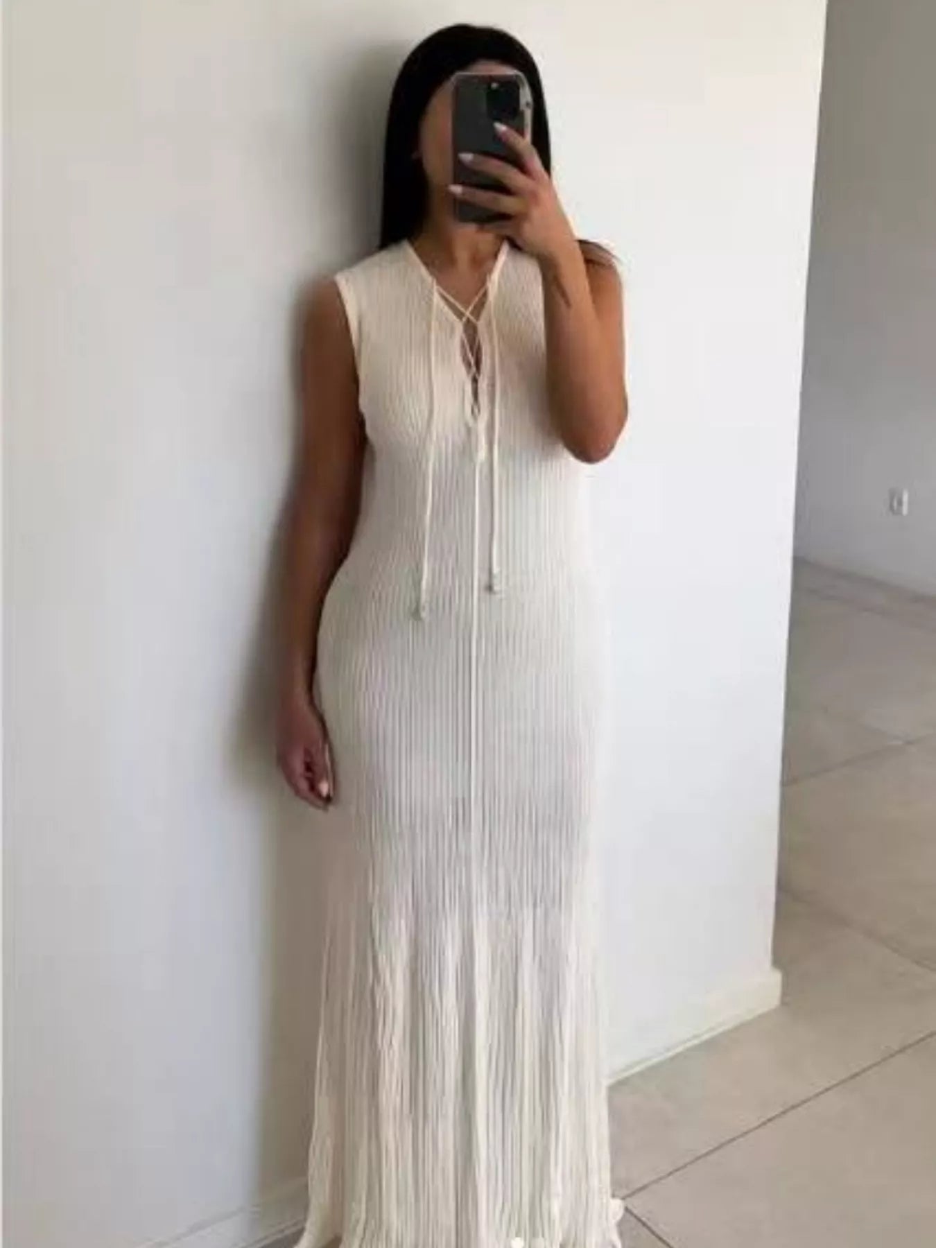 White ribbed sleeveless maxi dress with lace-up plunging neckline, styled indoors with a modern living room background.