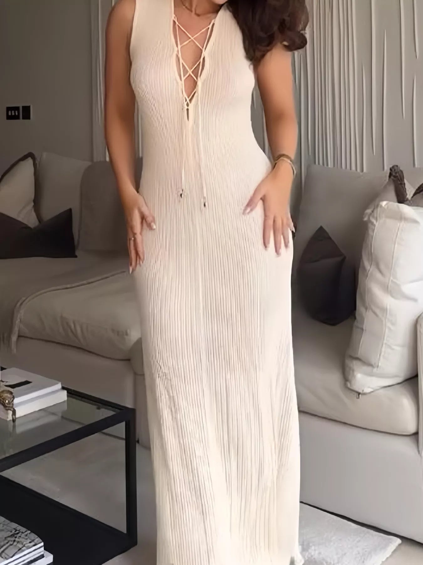 White ribbed sleeveless maxi dress with lace-up plunging neckline, styled indoors with a modern living room background.