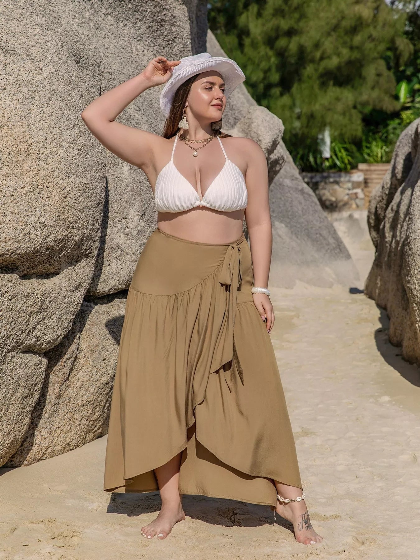 Flowy tan wrap maxi skirt with tie waist, ruffled hem, and slit detail, styled for a beach look.