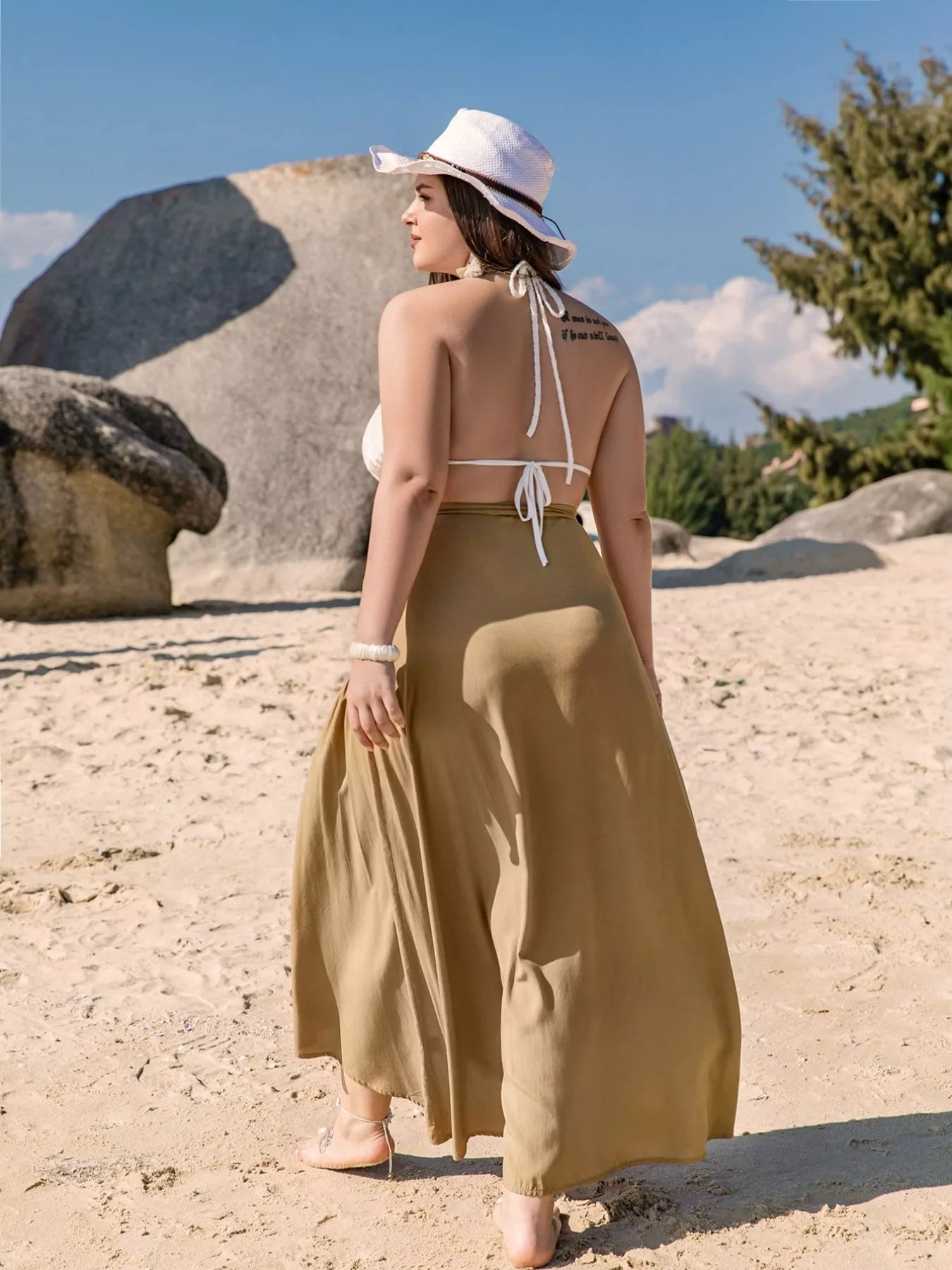 Flowy tan wrap maxi skirt with tie waist, ruffled hem, and slit detail, styled for a beach look.