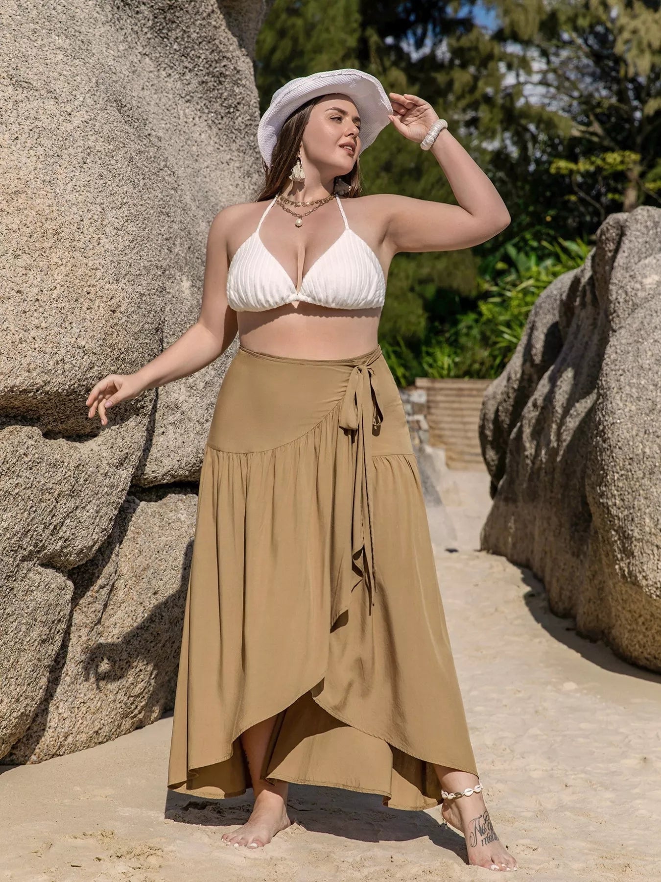 Flowy tan wrap maxi skirt with tie waist, ruffled hem, and slit detail, styled for a beach look.