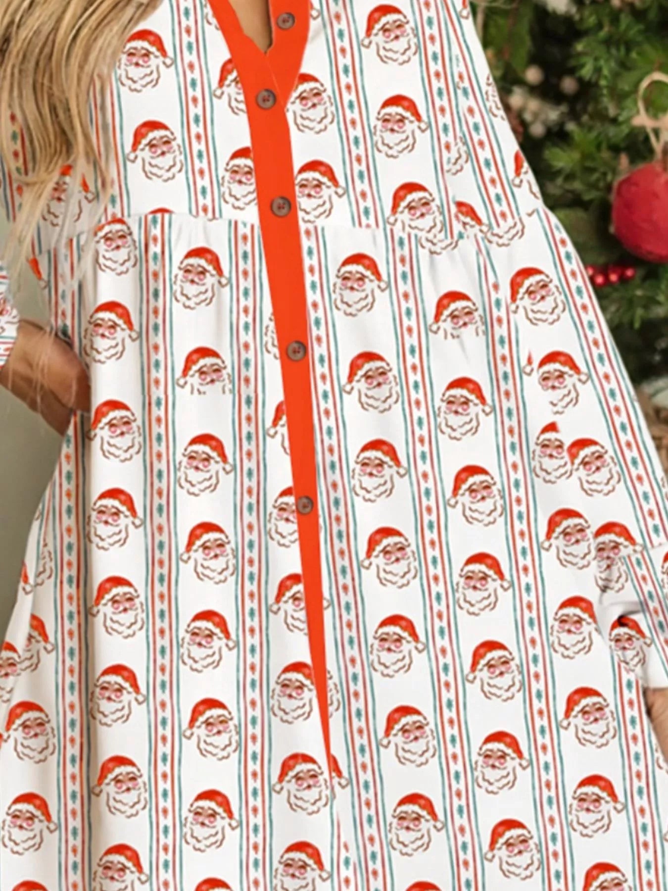 White swing dress with vertical Santa print stripes and red button placket, worn beside a decorated Christmas tree.
