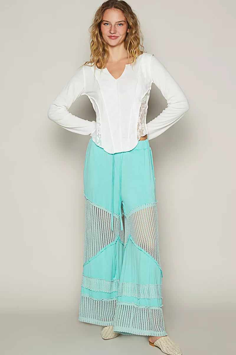 Model wearing seafoam aqua wide-leg pants with crochet mesh panels and drawstring waistband, styled with woven flats and a white top.