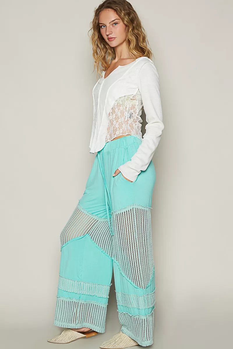 Model wearing seafoam aqua wide-leg pants with crochet mesh panels and drawstring waistband, styled with woven flats and a white top.