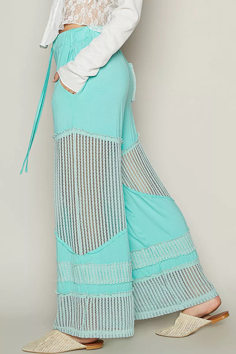 Model wearing seafoam aqua wide-leg pants with crochet mesh panels and drawstring waistband, styled with woven flats and a white top.