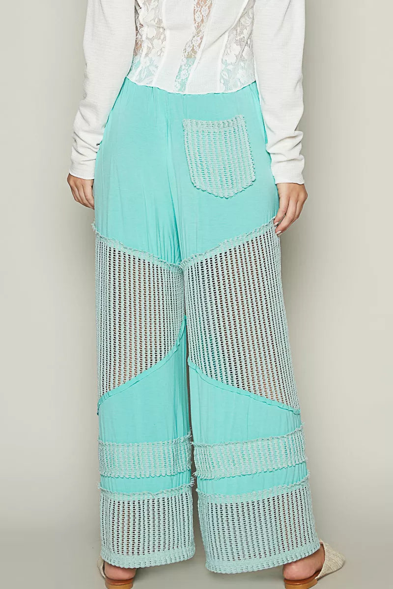 Model wearing seafoam aqua wide-leg pants with crochet mesh panels and drawstring waistband, styled with woven flats and a white top.