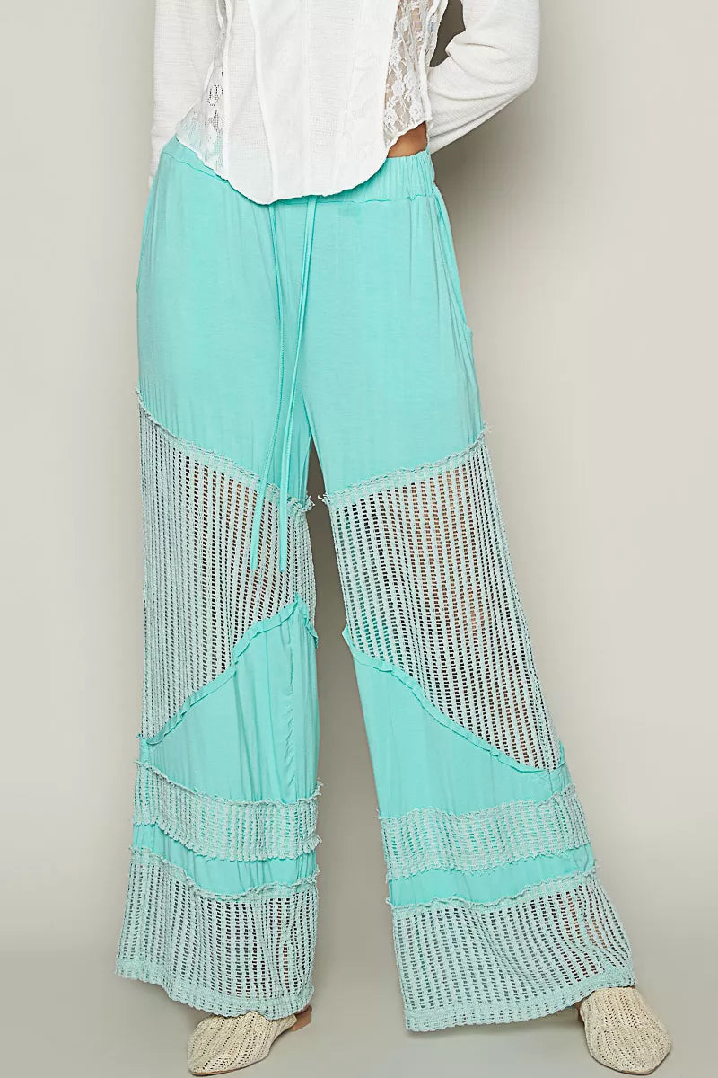 Model wearing seafoam aqua wide-leg pants with crochet mesh panels and drawstring waistband, styled with woven flats and a white top.