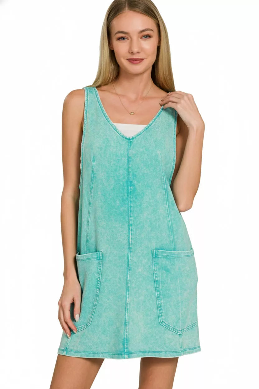 Model wearing a seafoam acid-washed overall mini dress with a sleeveless silhouette and front pockets.