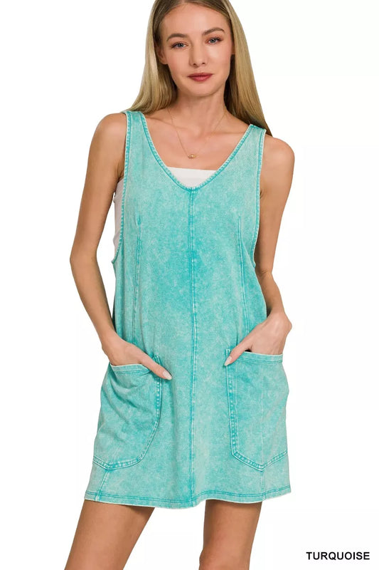 Model wearing a seafoam acid-washed overall mini dress with a sleeveless silhouette and front pockets.
