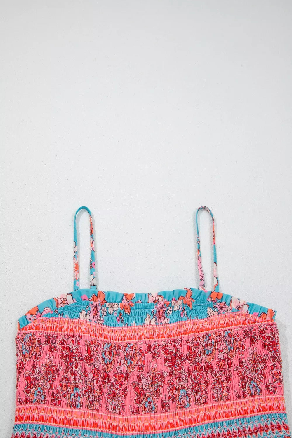 Blue floral smocked maxi dress with spaghetti straps, pink border detailing, and hidden pockets worn on the beach.