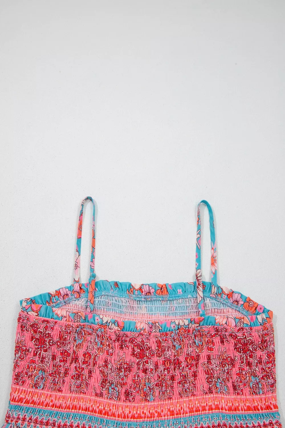 Blue floral smocked maxi dress with spaghetti straps, pink border detailing, and hidden pockets worn on the beach.