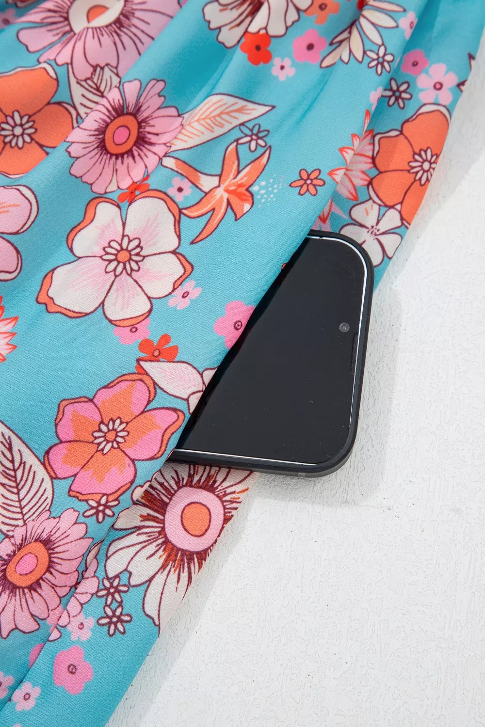 Blue floral smocked maxi dress with spaghetti straps, pink border detailing, and hidden pockets worn on the beach.