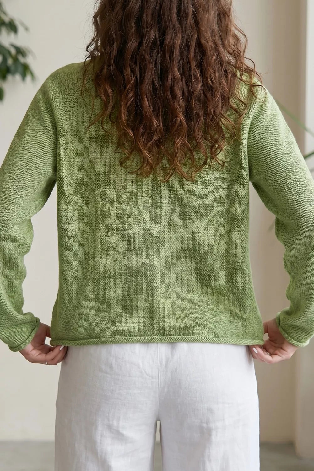 Green knit sweater with a blue fish graphic, ribbed detail, long sleeves, and relaxed slightly stretchy fit styled with white pants.