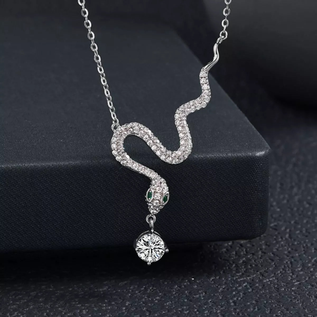 Sterling silver snake pendant necklace with a moissanite drop and green accent eyes.