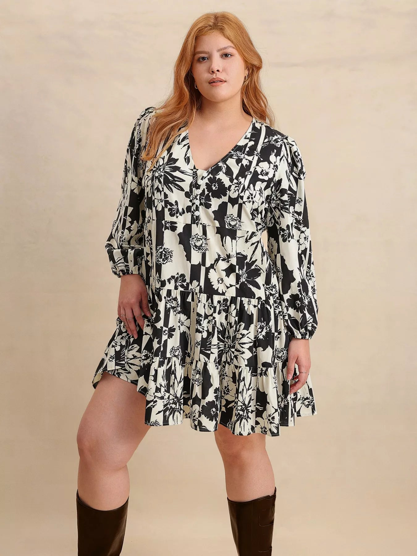 Plus size model wearing the Shadow Petals Mini Dress, a black-and-white floral print mini dress with long sleeves, ruched details, and a flowy hemline, styled with knee-high boots.