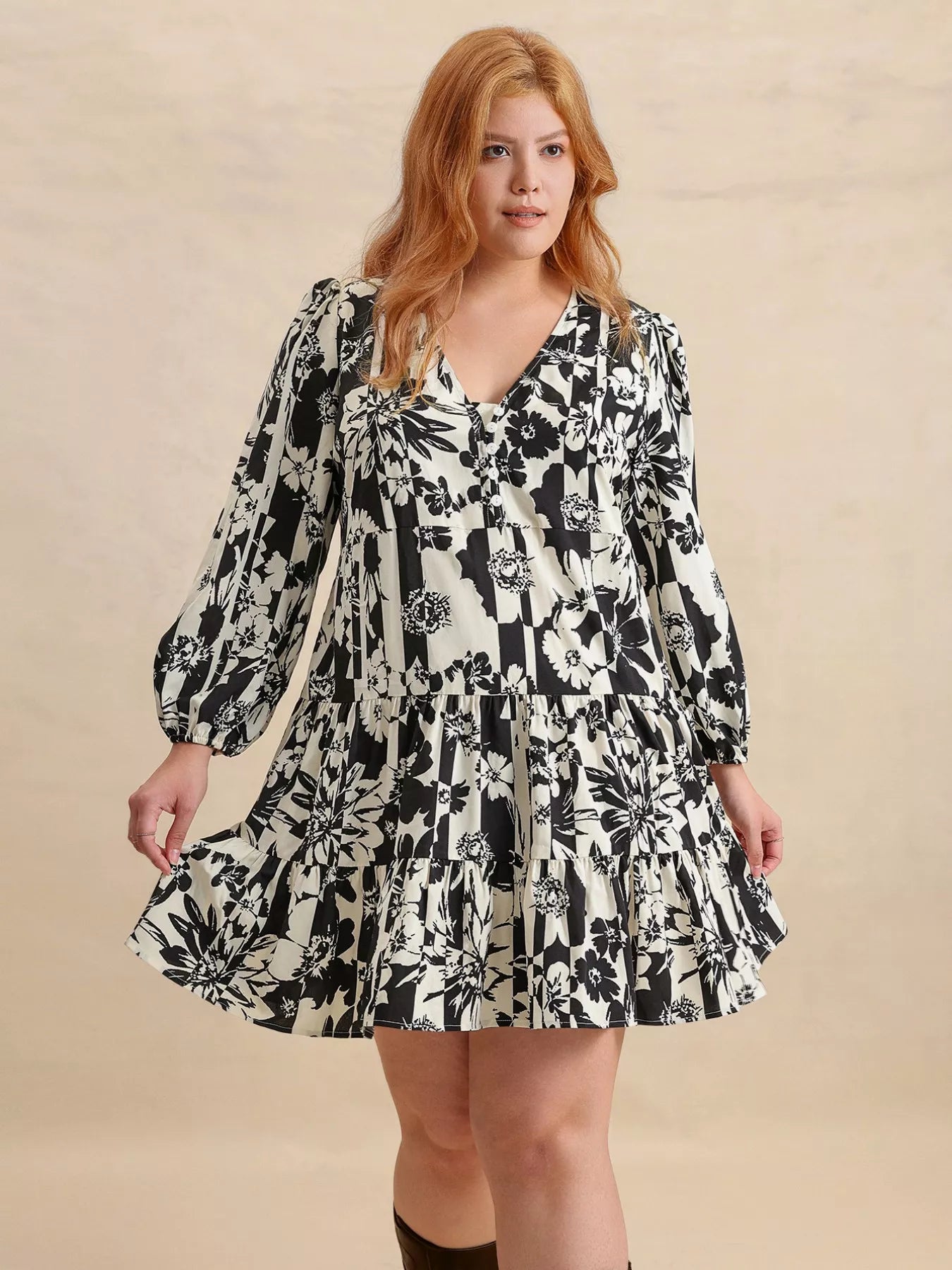 Plus size model wearing the Shadow Petals Mini Dress, a black-and-white floral print mini dress with long sleeves, ruched details, and a flowy hemline, styled with knee-high boots.