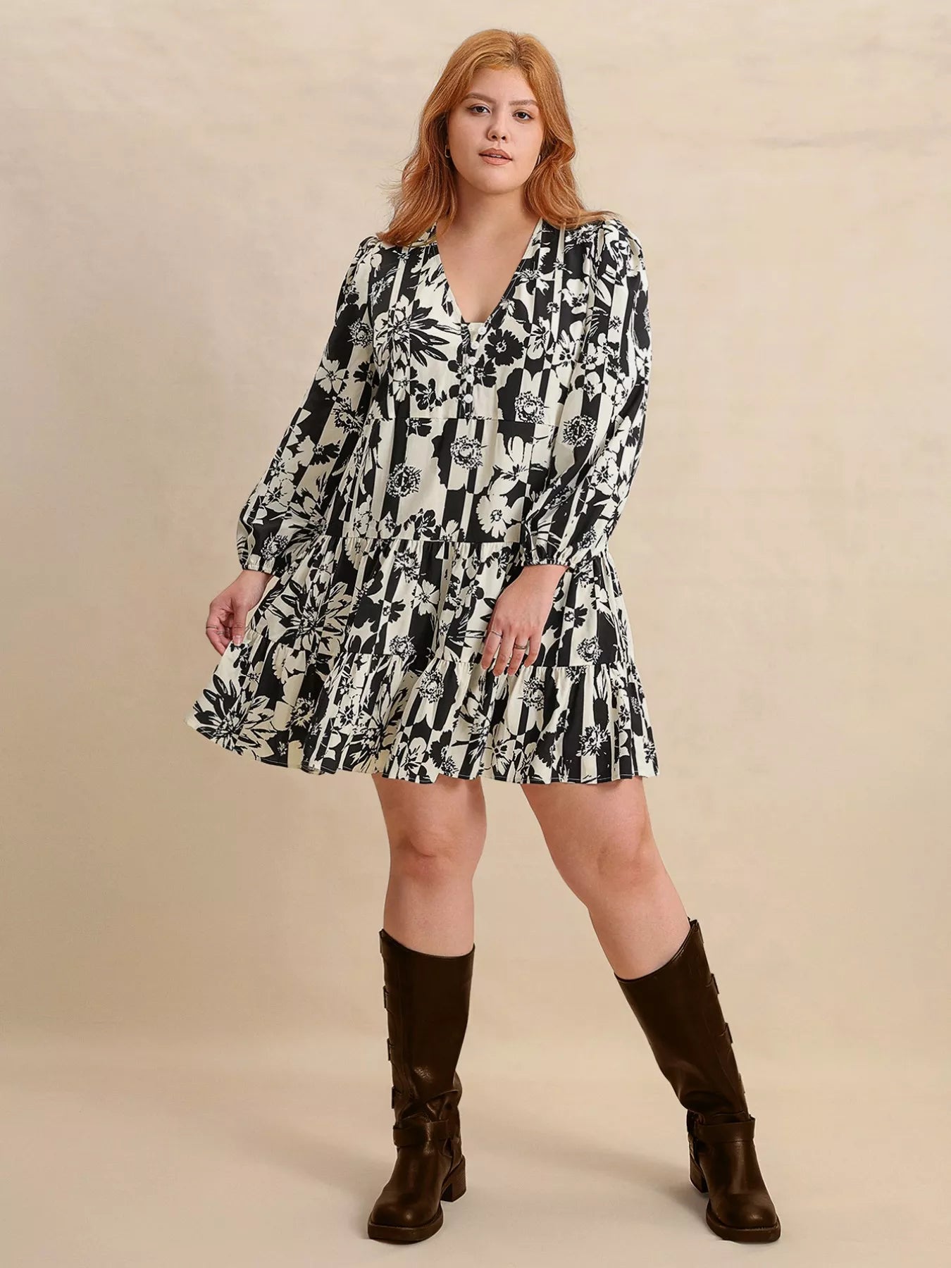 Plus size model wearing the Shadow Petals Mini Dress, a black-and-white floral print mini dress with long sleeves, ruched details, and a flowy hemline, styled with knee-high boots.