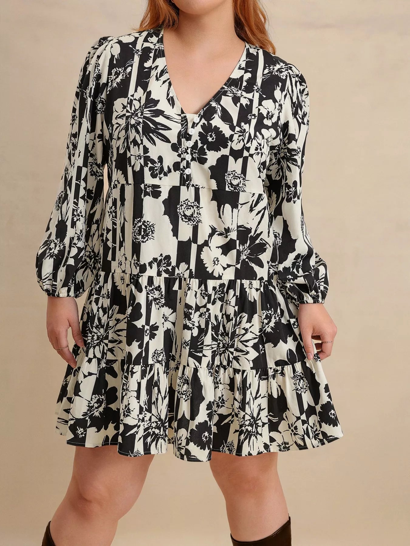 Plus size model wearing the Shadow Petals Mini Dress, a black-and-white floral print mini dress with long sleeves, ruched details, and a flowy hemline, styled with knee-high boots.