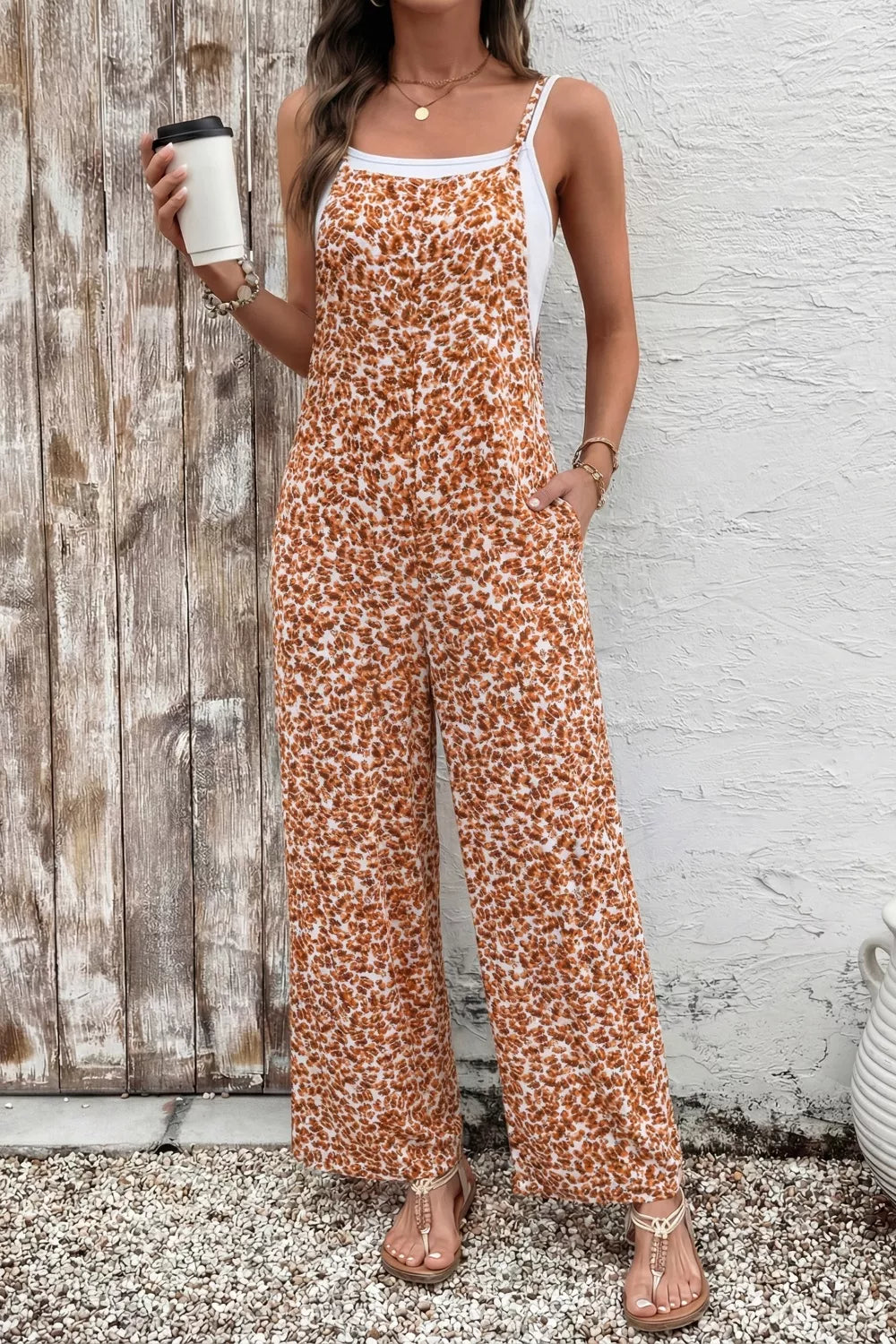 Orange floral wide-leg jumpsuit with thin straps, relaxed flowy fit, and side pockets styled with sandals.