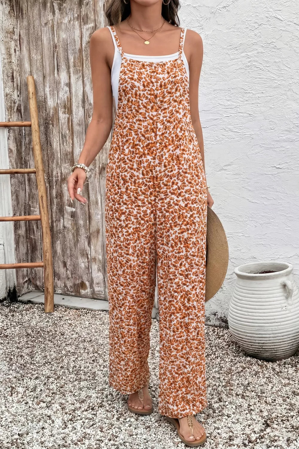 Orange floral wide-leg jumpsuit with thin straps, relaxed flowy fit, and side pockets styled with sandals.