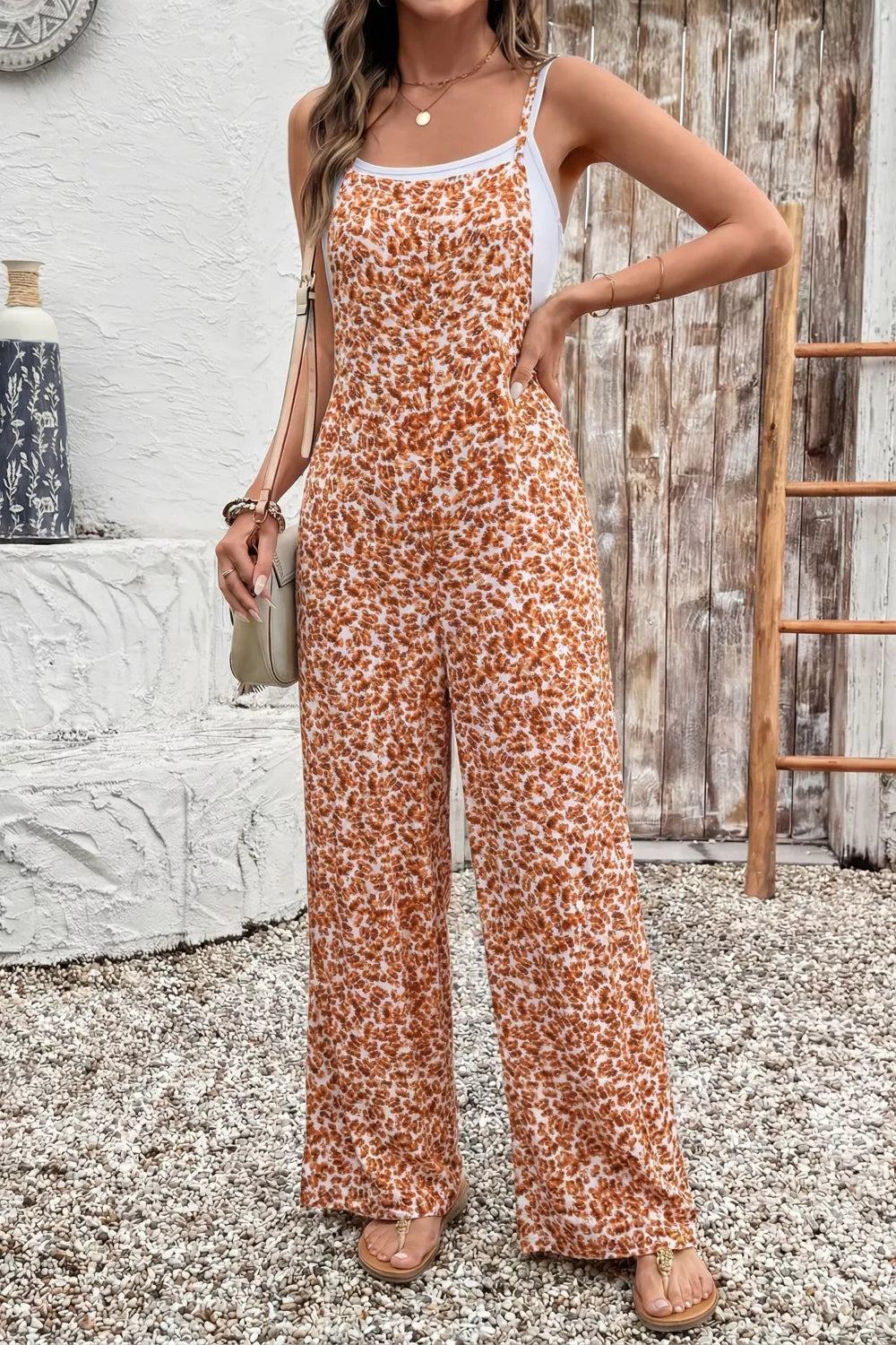 Orange floral wide-leg jumpsuit with thin straps, relaxed flowy fit, and side pockets styled with sandals.
