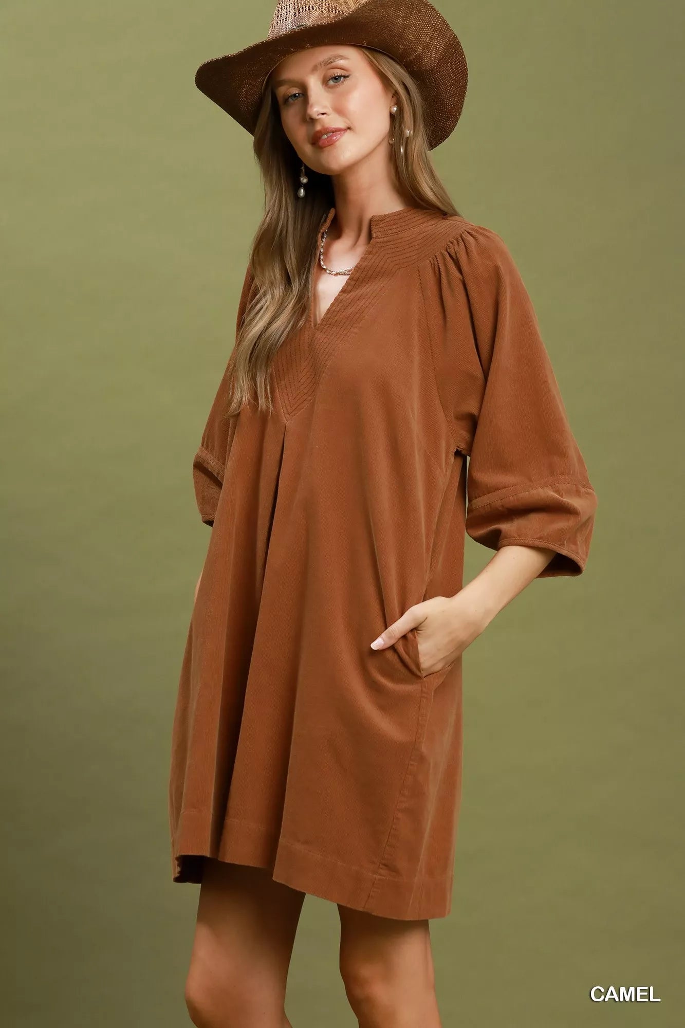 Camel corduroy shift dress with V-neckline, puff sleeves, side pockets, and relaxed fit styled with a wide-brim hat.