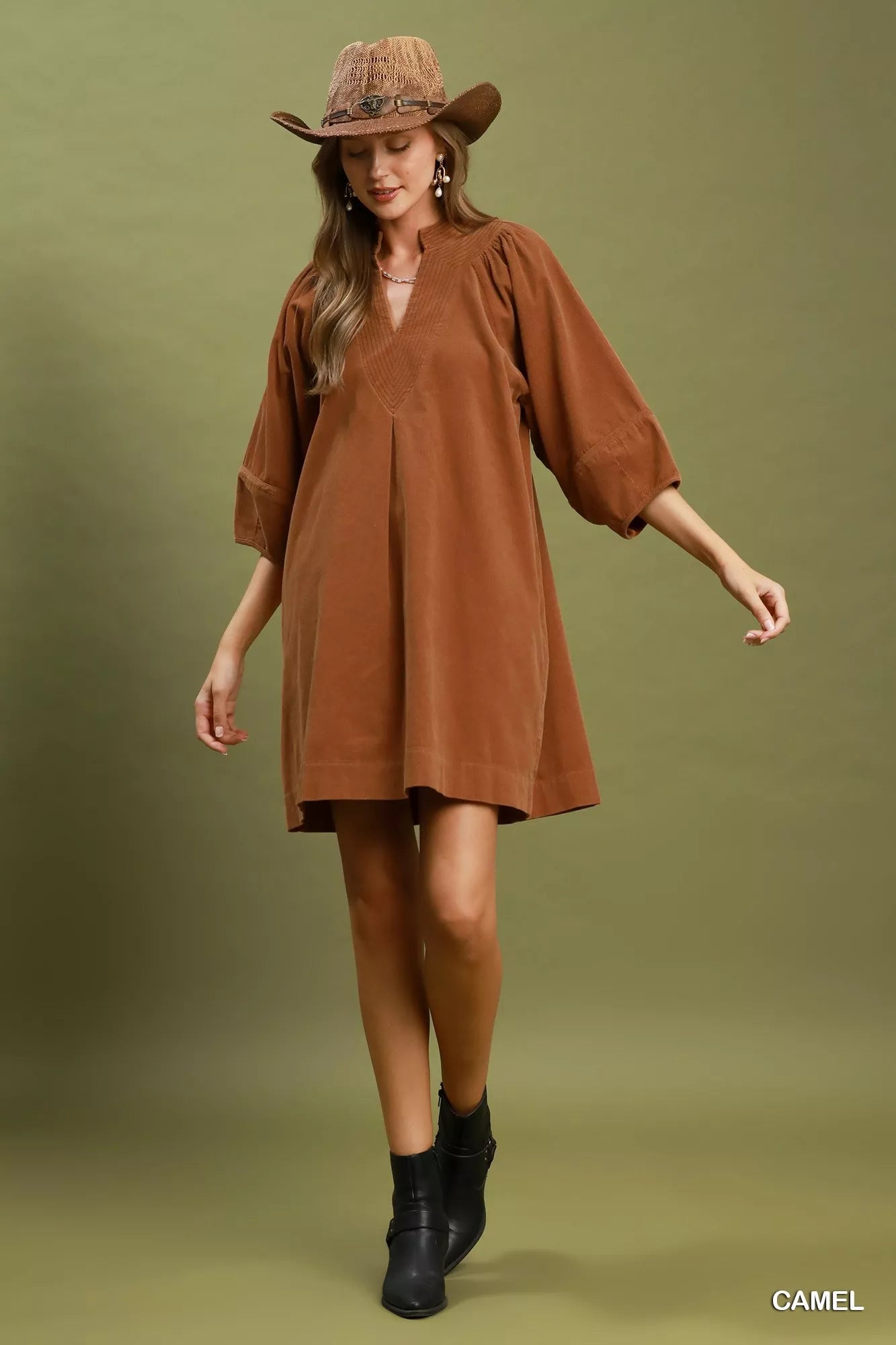 Camel corduroy shift dress with V-neckline, puff sleeves, side pockets, and relaxed fit styled with a wide-brim hat.