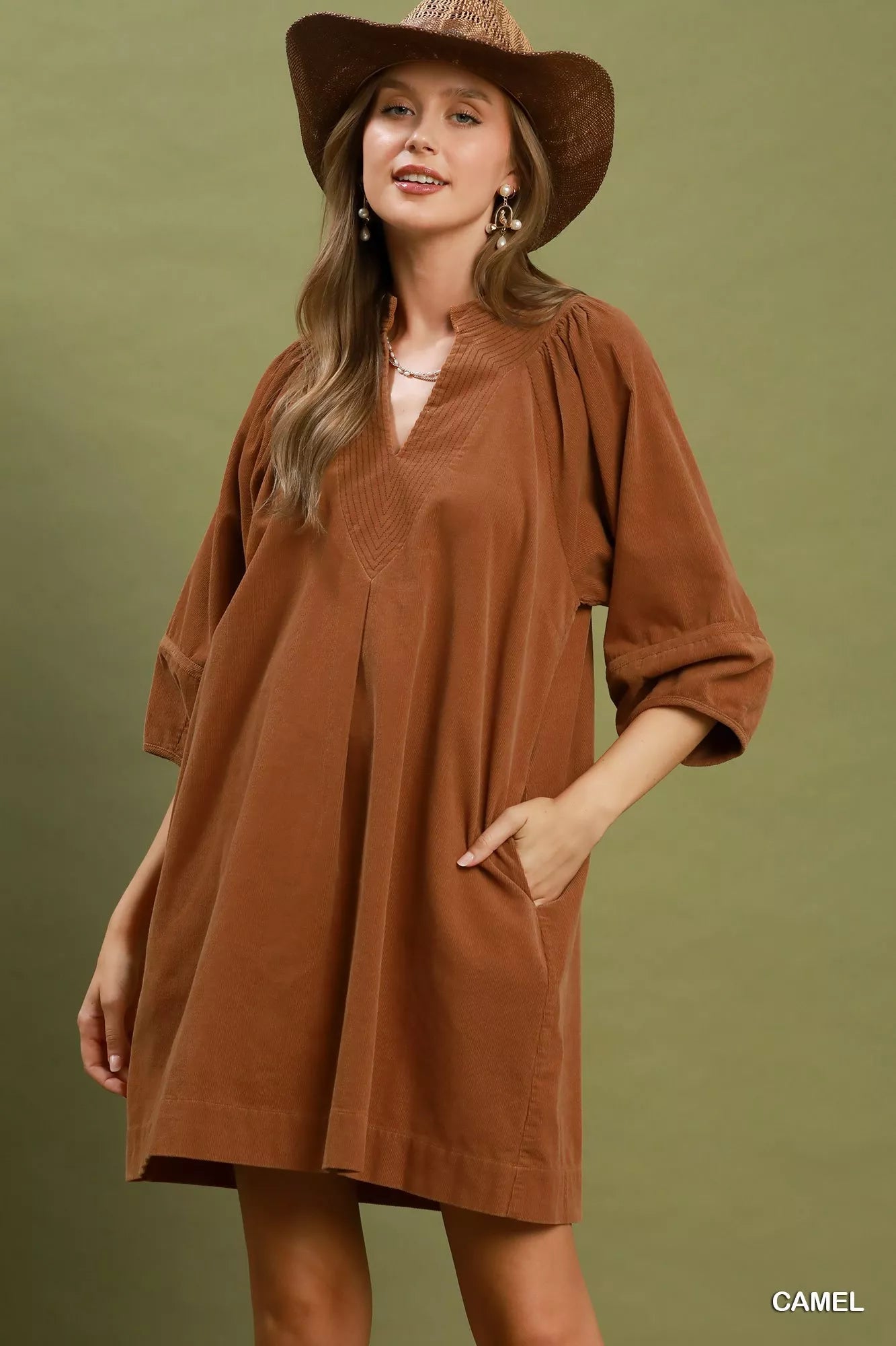 Camel corduroy shift dress with V-neckline, puff sleeves, side pockets, and relaxed fit styled with a wide-brim hat.