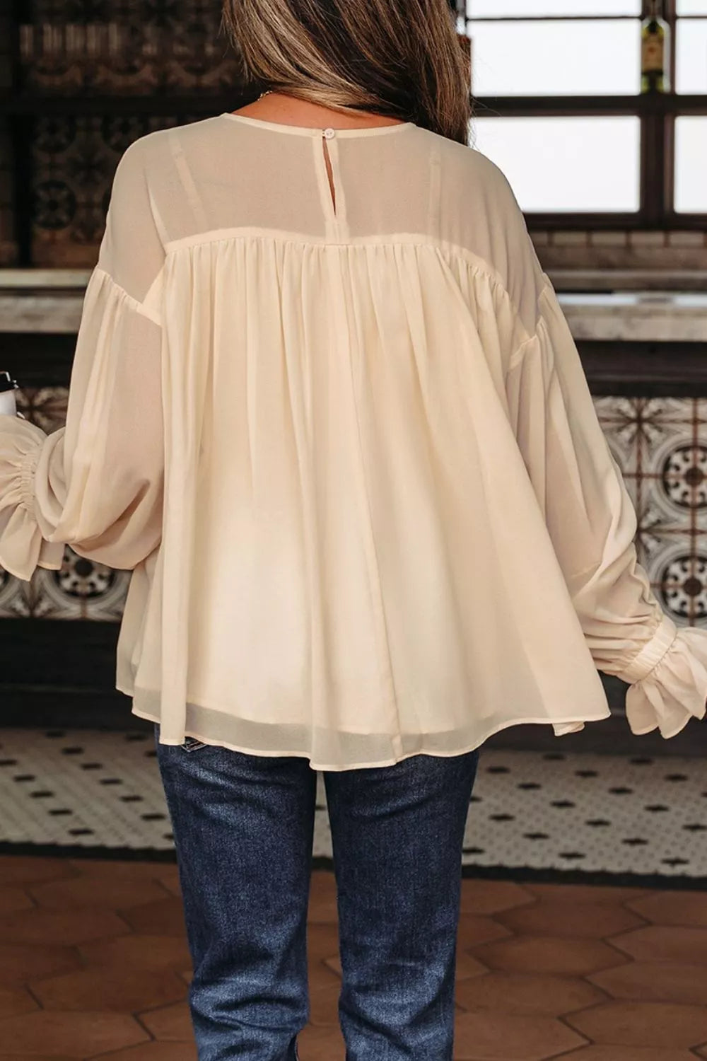 Flowy ruffle sleeve blouse with a relaxed silhouette styled with jeans and a casual coffee cup.