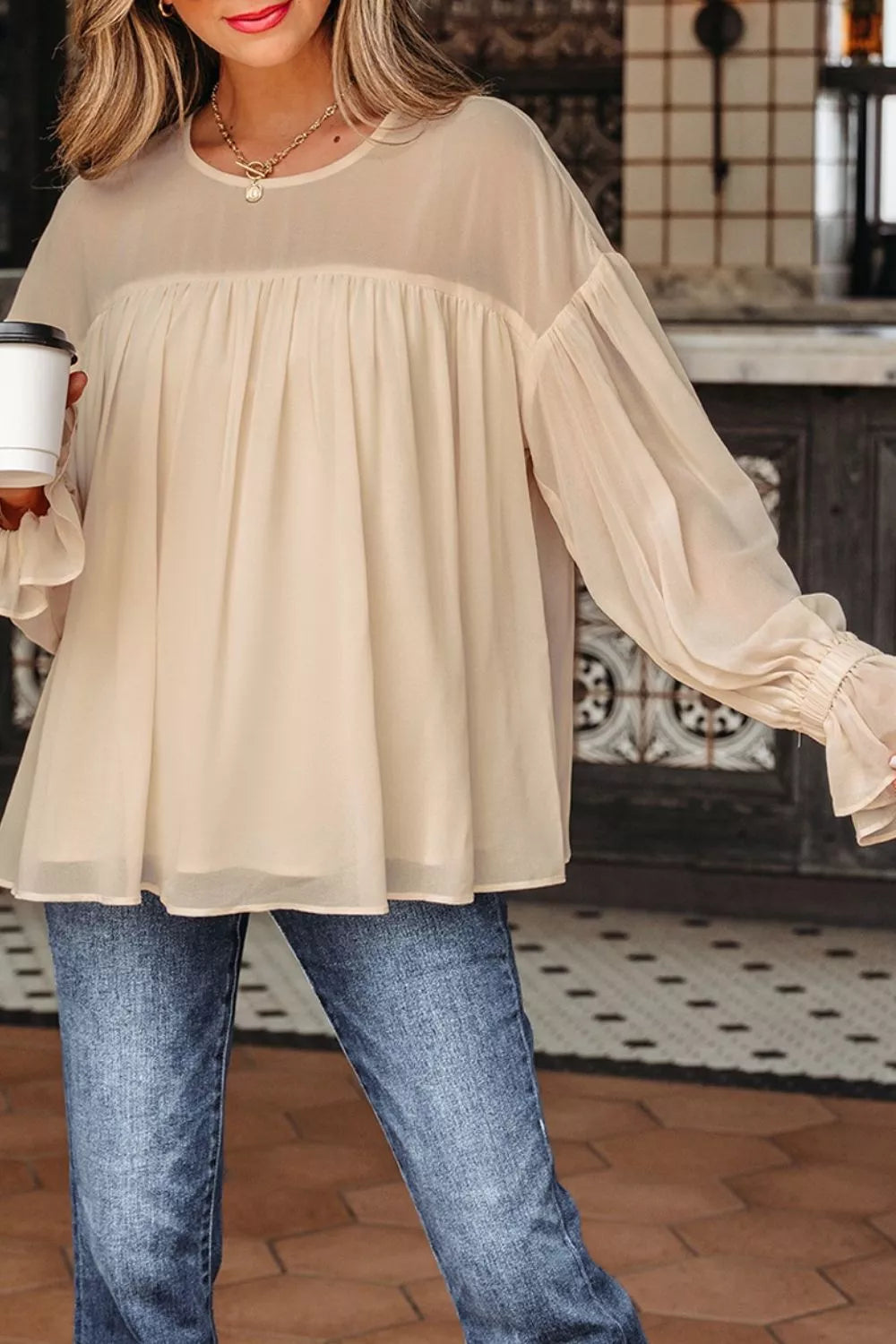 Flowy ruffle sleeve blouse with a relaxed silhouette styled with jeans and a casual coffee cup.