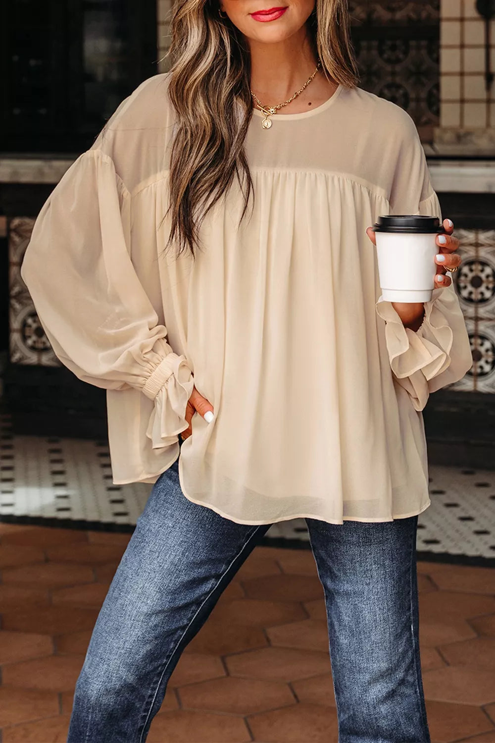 Flowy ruffle sleeve blouse with a relaxed silhouette styled with jeans and a casual coffee cup.