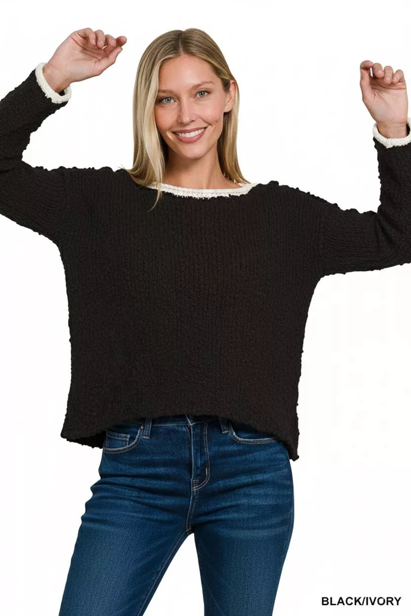 Model wearing the Solar Eclipse Contrast Sweater — a black textured cropped knit with ivory trim on the neckline and cuffs, styled with denim jeans.