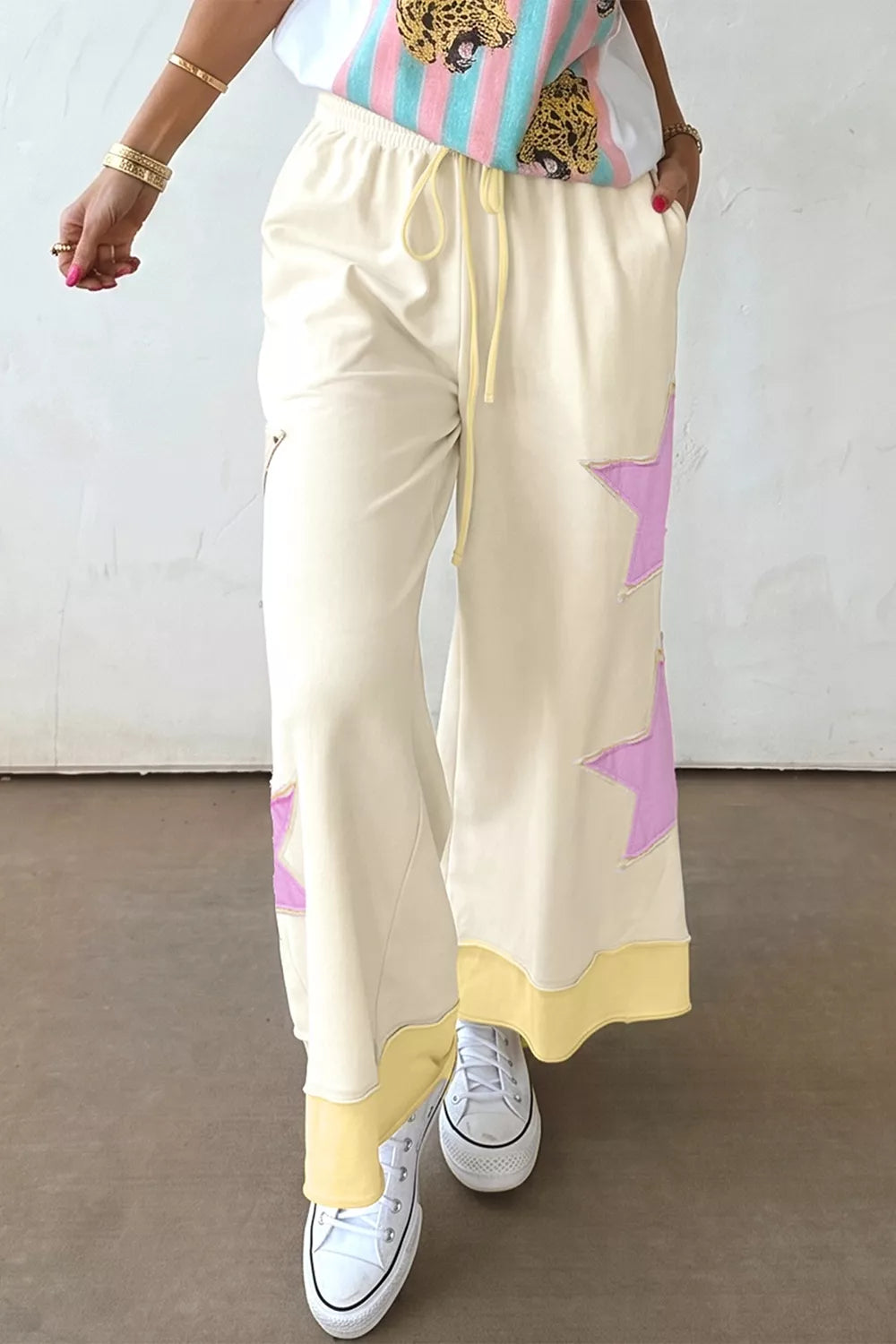 Cream wide leg pants with pastel star patch details, drawstring waist, pockets, and soft cotton-blend fabric styled with sneakers.