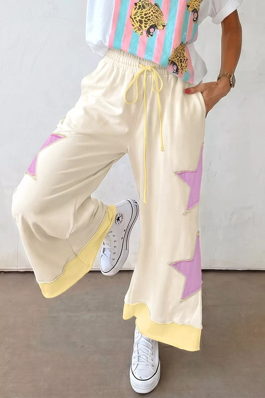 Cream wide leg pants with pastel star patch details, drawstring waist, pockets, and soft cotton-blend fabric styled with sneakers.