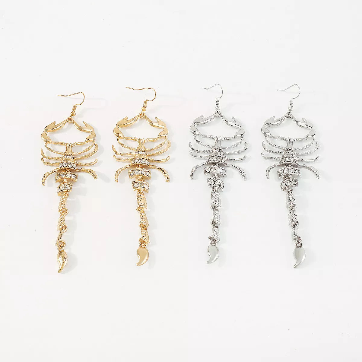 Gold and silver scorpion-shaped rhinestone statement earrings with ribbed detailing displayed on a white surface.