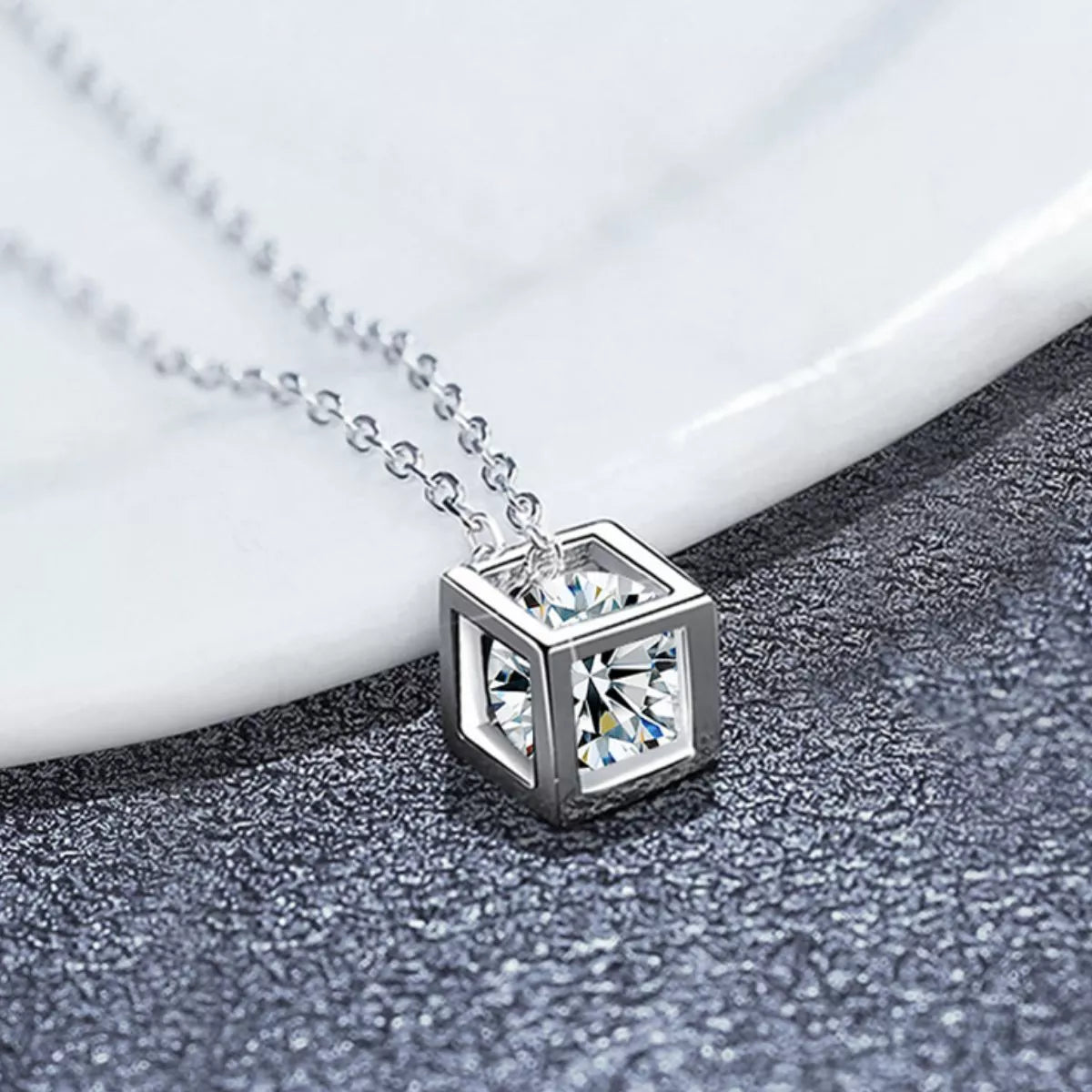 Platinum plated sterling silver geometric pendant necklace featuring a sparkling moissanite stone on a dark textured background