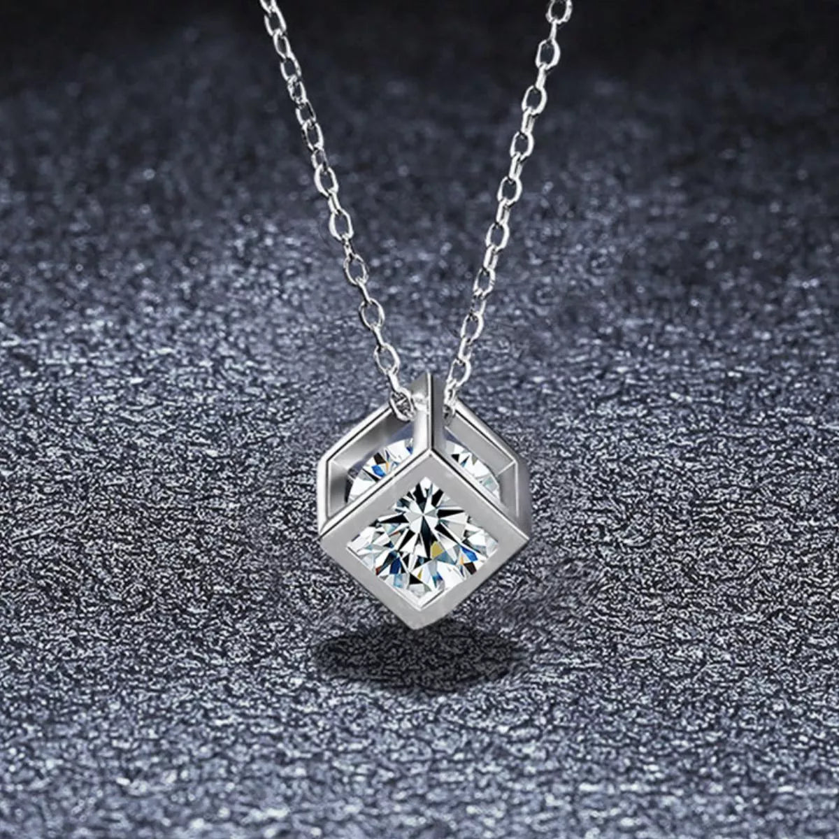 Platinum plated sterling silver geometric pendant necklace featuring a sparkling moissanite stone on a dark textured background