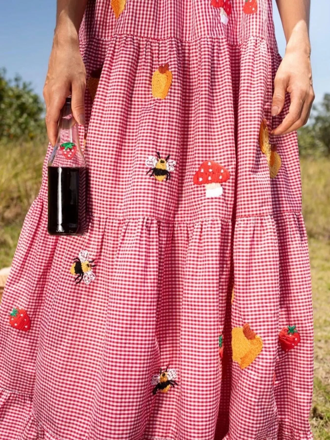 Woman in red gingham maxi dress with embroidered strawberries, bees, and mushrooms