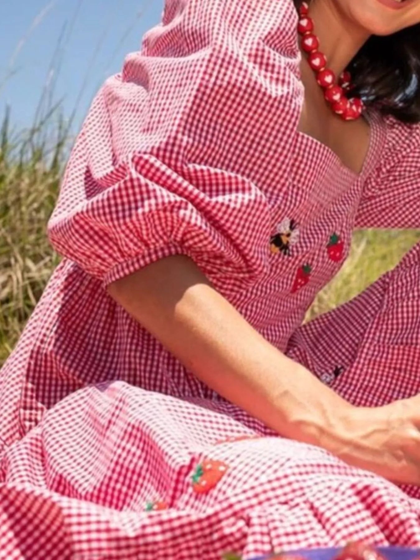 Woman in red gingham maxi dress with embroidered strawberries, bees, and mushrooms
