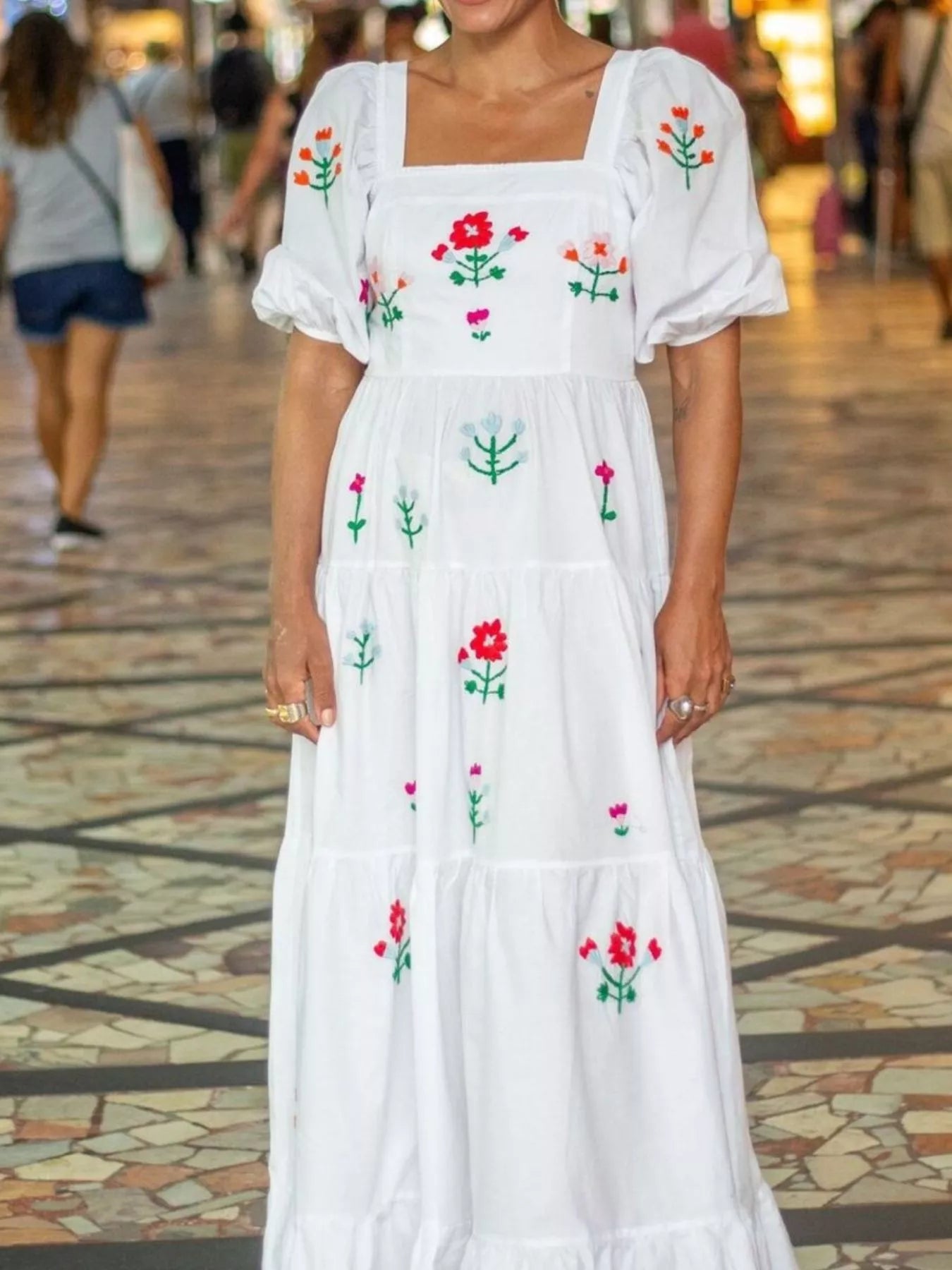 White maxi dress with colorful floral embroidery, square neckline, and ruffled tiers