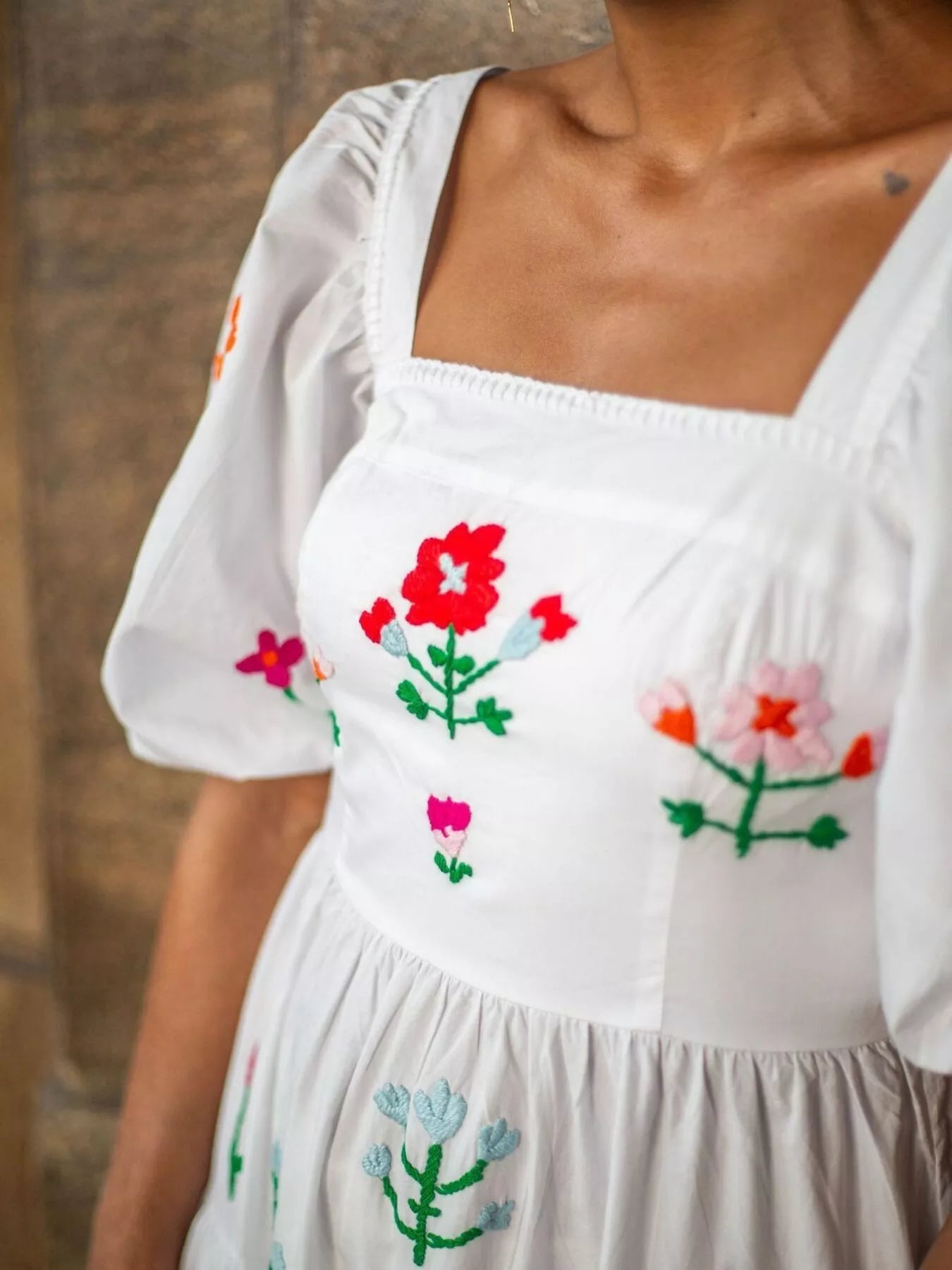 White maxi dress with colorful floral embroidery, square neckline, and ruffled tiers