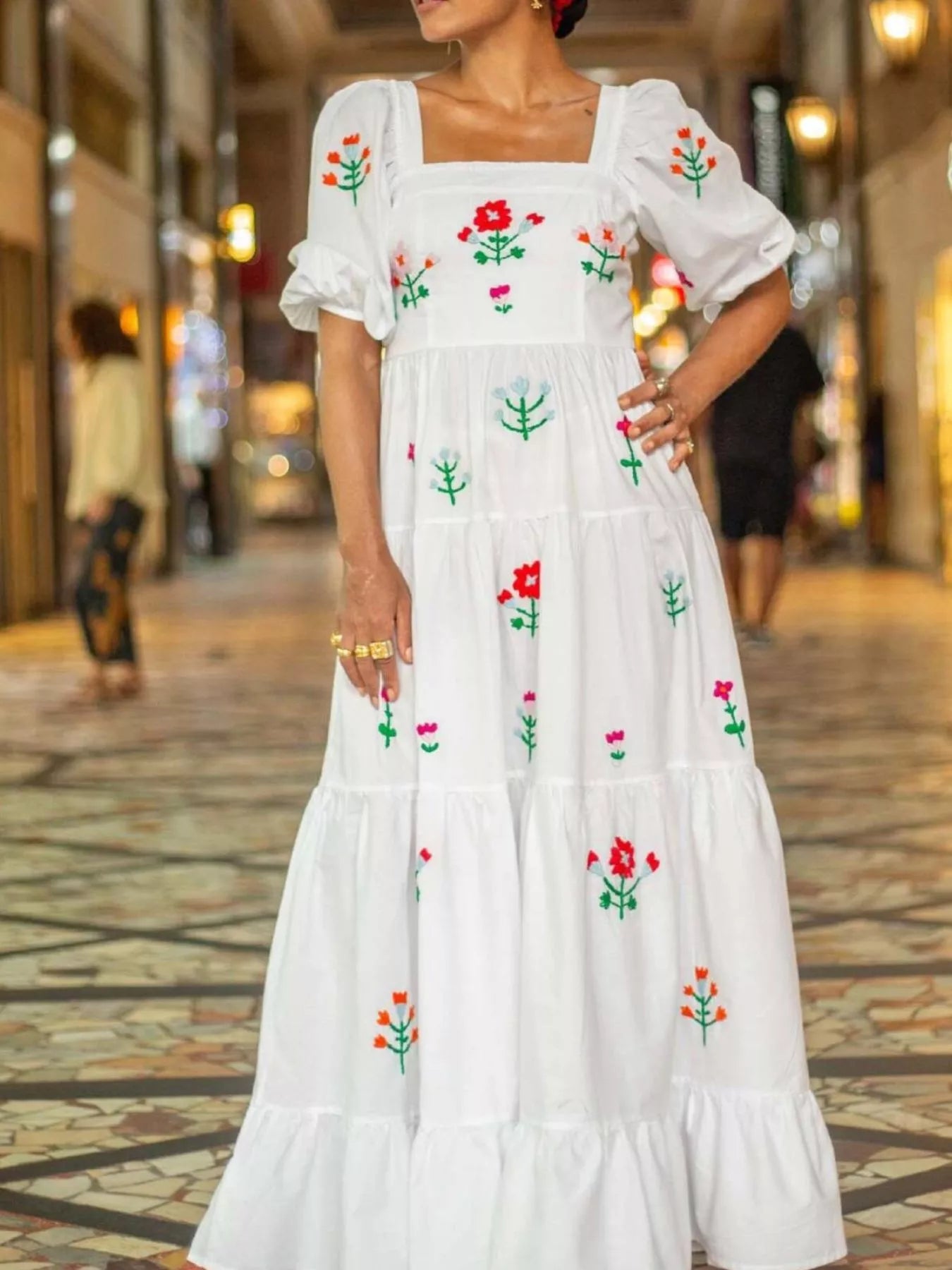 White maxi dress with colorful floral embroidery, square neckline, and ruffled tiers