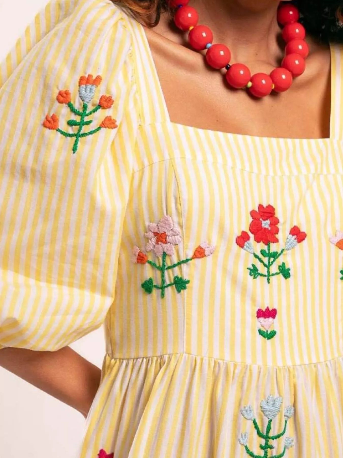 Woman wearing yellow striped maxi dress with colorful floral embroidery and puff sleeves