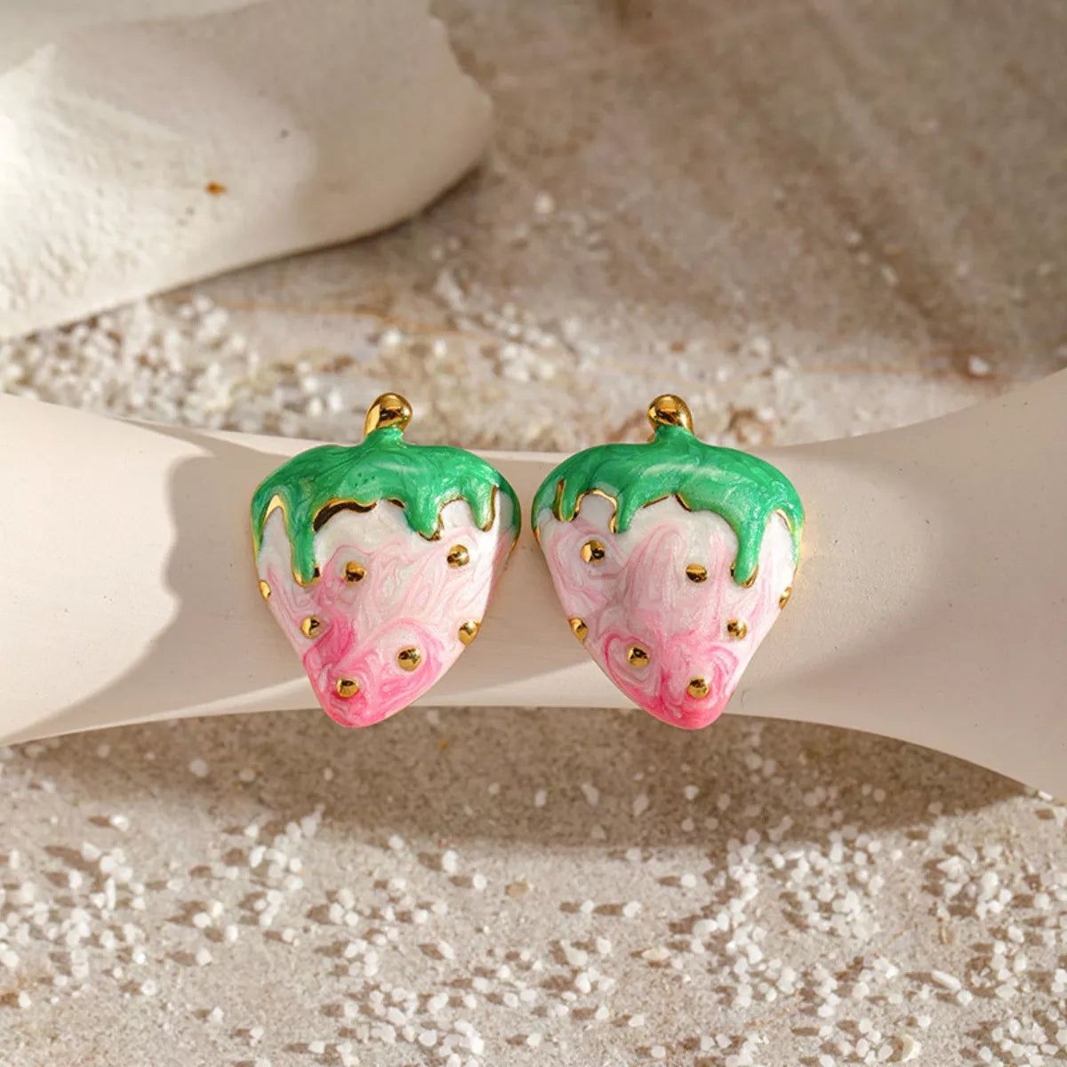 Pink and green strawberry stud earrings with gold accents on a neutral background