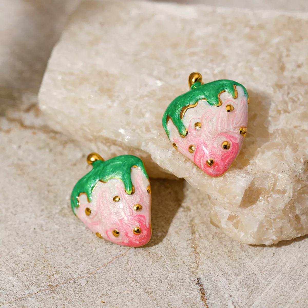 Pink and green strawberry stud earrings with gold accents on a neutral background