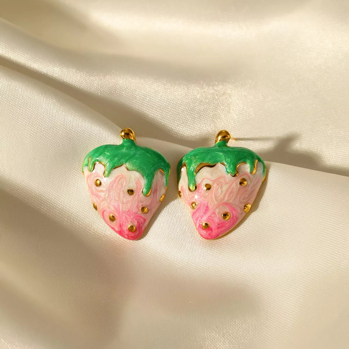 Pink and green strawberry stud earrings with gold accents on a neutral background